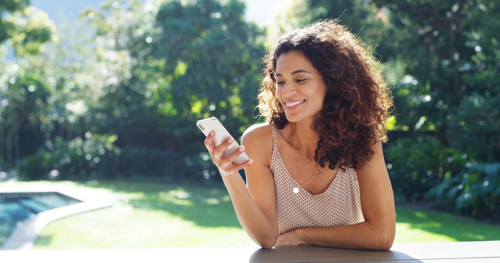 A woman smiling at her phone outdoors